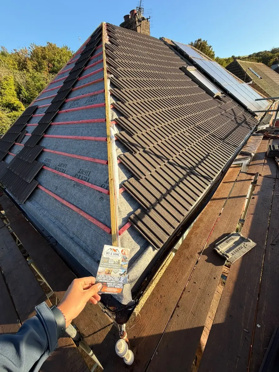 Dark tiles being laid up a hip roof, flyer in shot