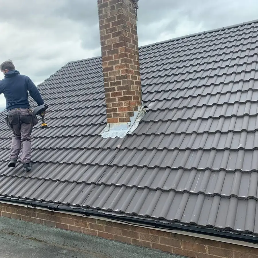 Roofer on a finished grey concrete tile roof beside a chimney