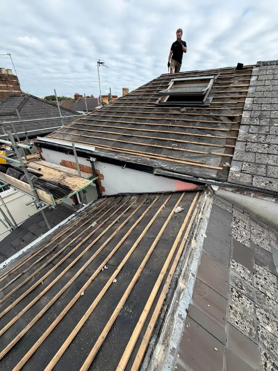 Roofer at the ridge of a roof stripped to the battens